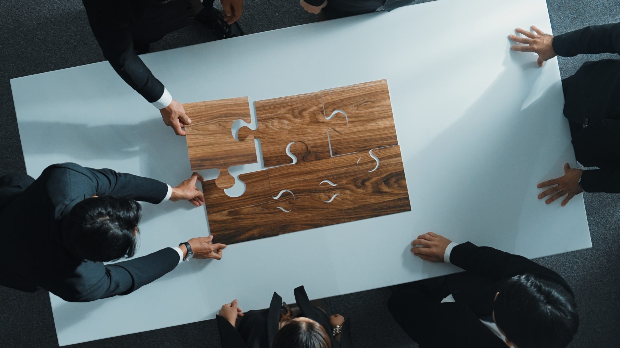 Top view of business people putting jigsaw together at meeting room. Professional marketing team standing at table while gathering puzzle piece. Show unity, cooperation and team working. Directorate.
